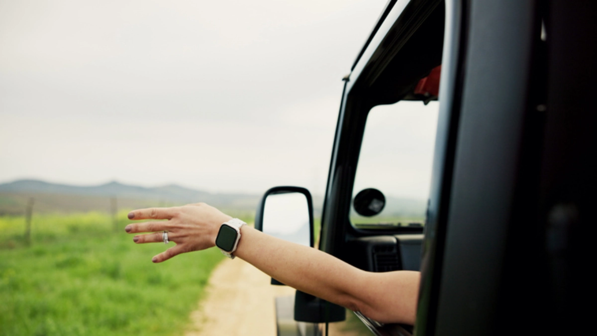 an image of a woman's hand out of a car window in rural countryside road