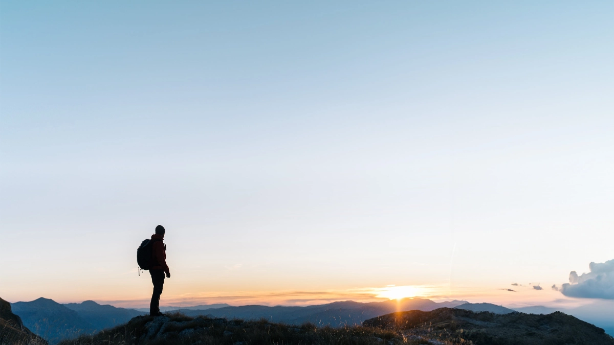 an image of a man watching the sun rise over a mountain peak