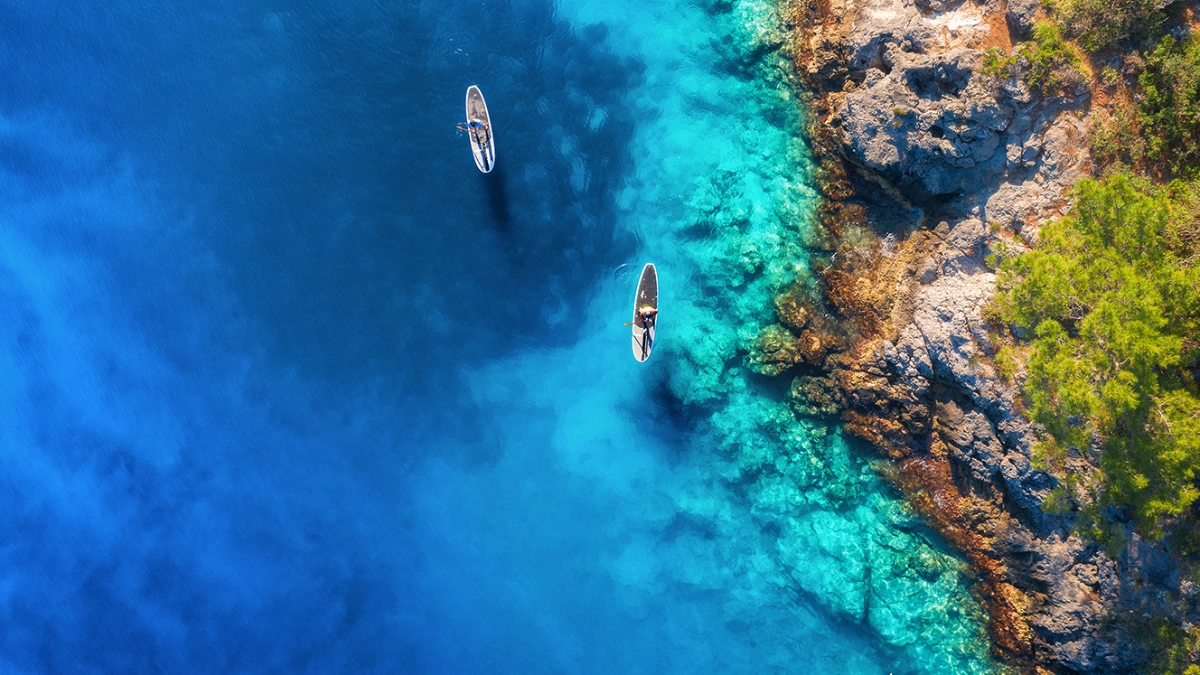 an overhead image of two people paddling boats near a coast