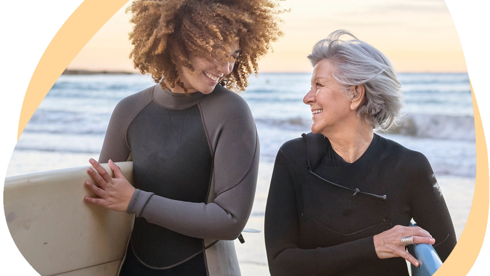 Two people holding surfboards and wearing wetsuits at the beach