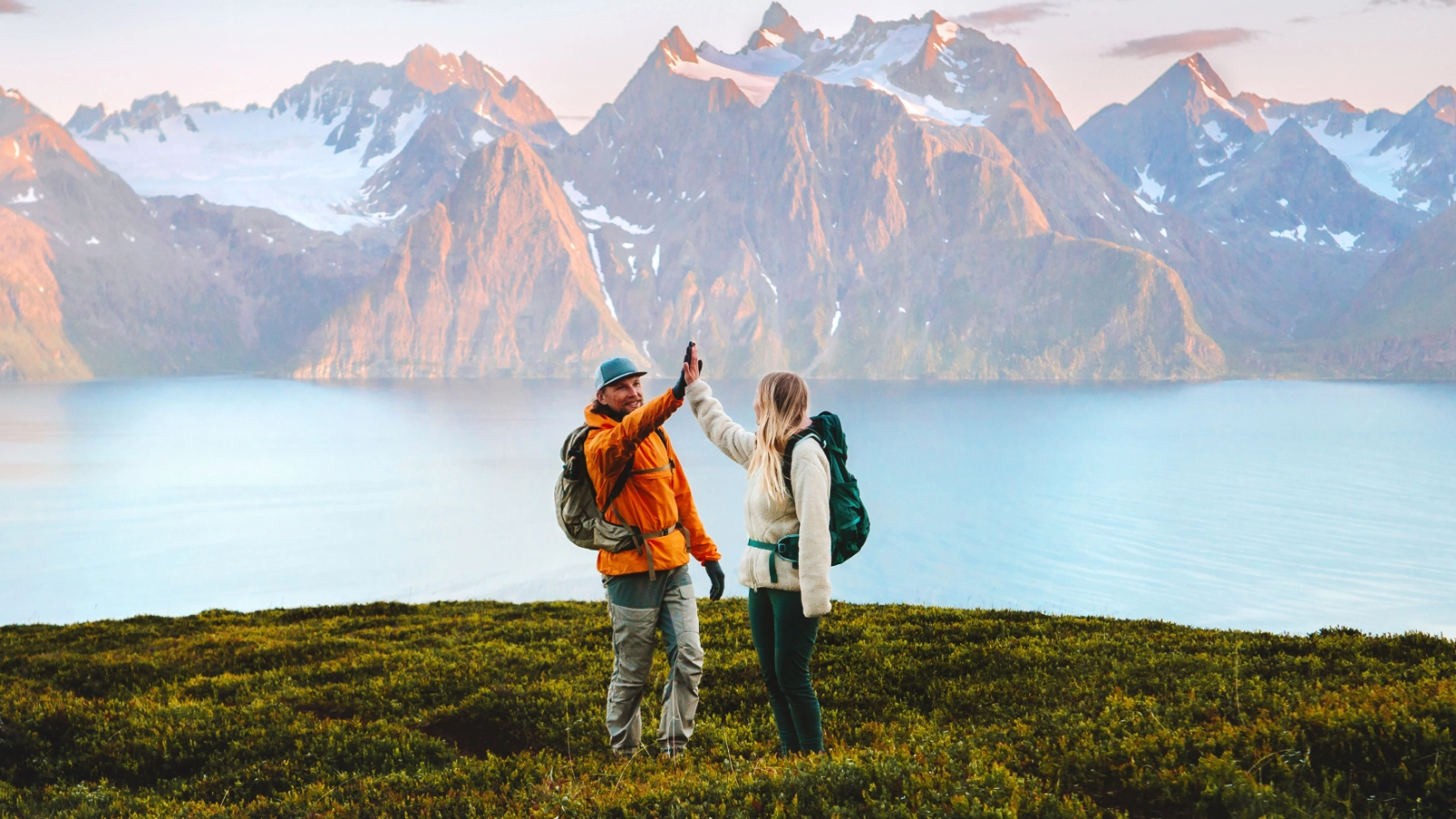 Two hikers with backpacks high-fiving on a hillside