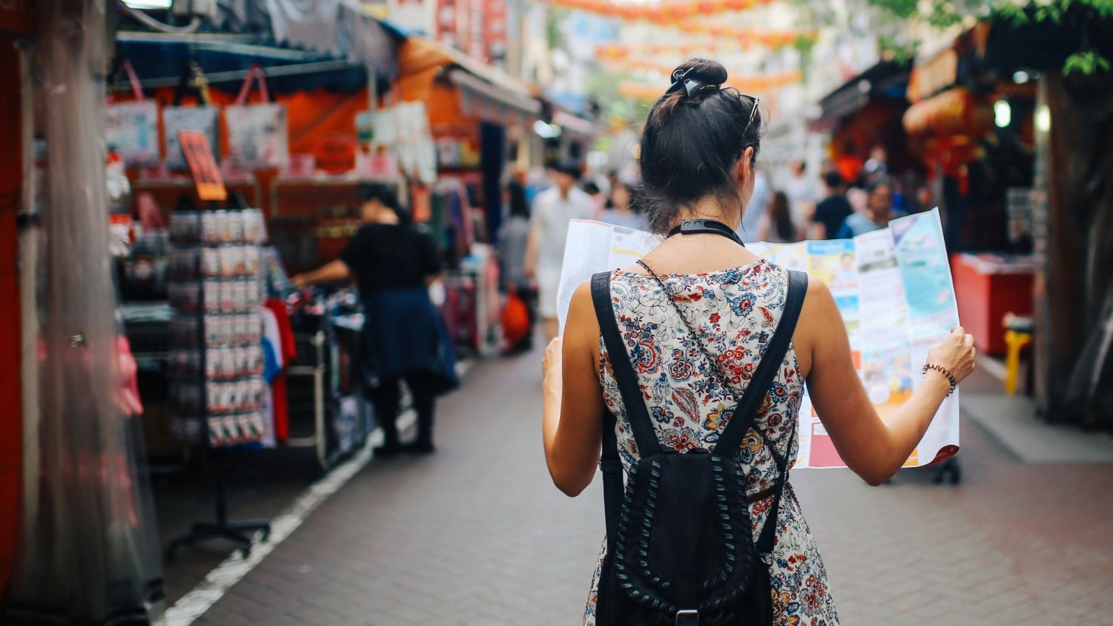 Young solo traveler woman in Singapore street market checking the map.