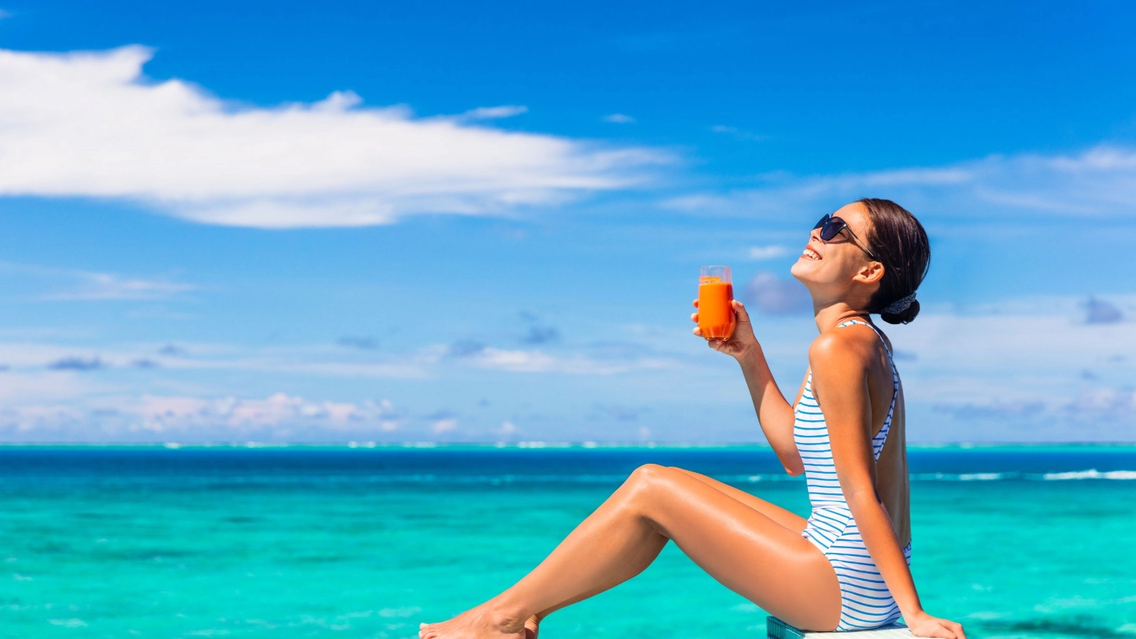 A girl enjoying sun tan holidays by the swimming pool of tropical hotel.