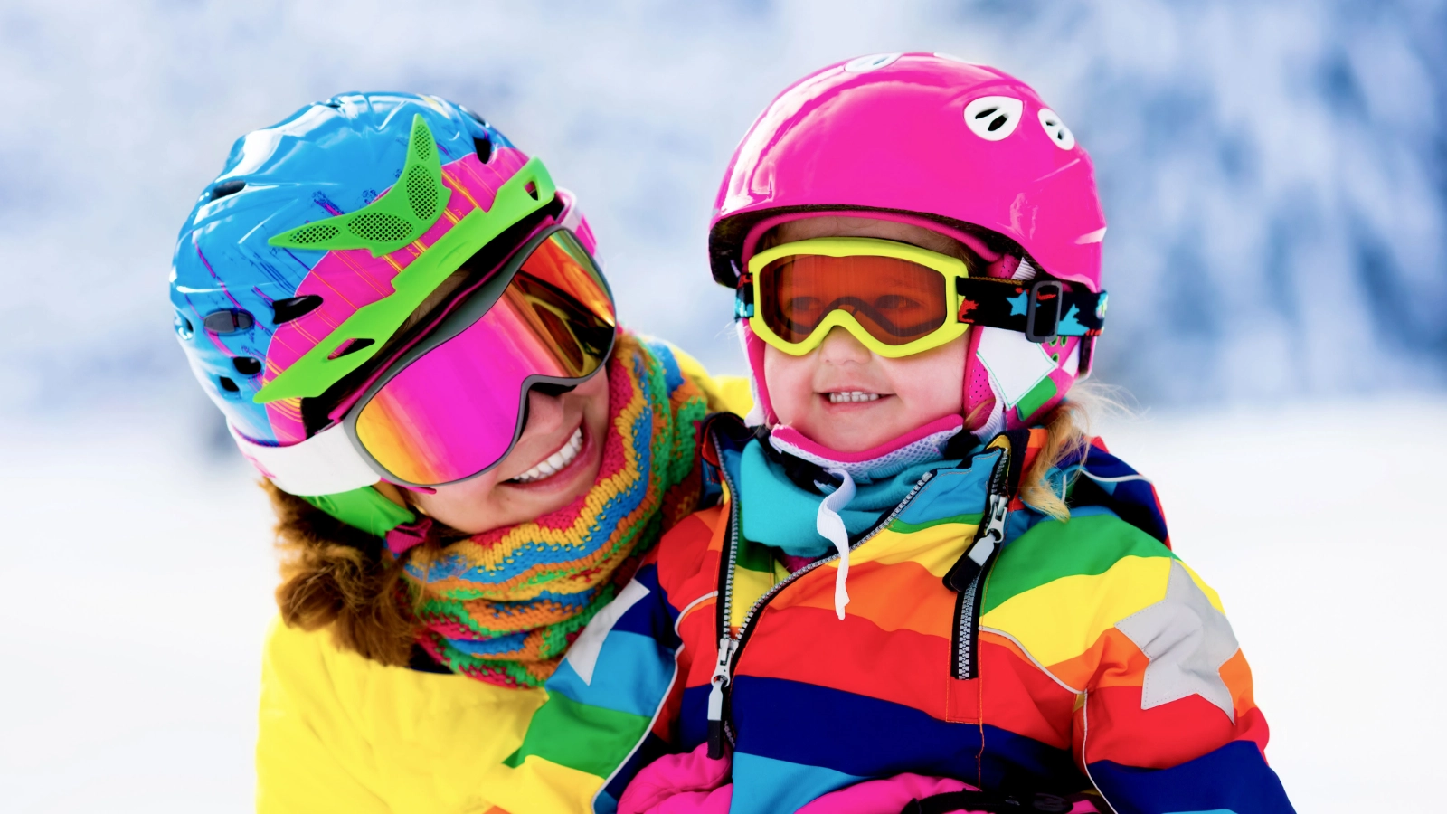 Two people in colourful ski gear smiling outdoors in a snowy setting.