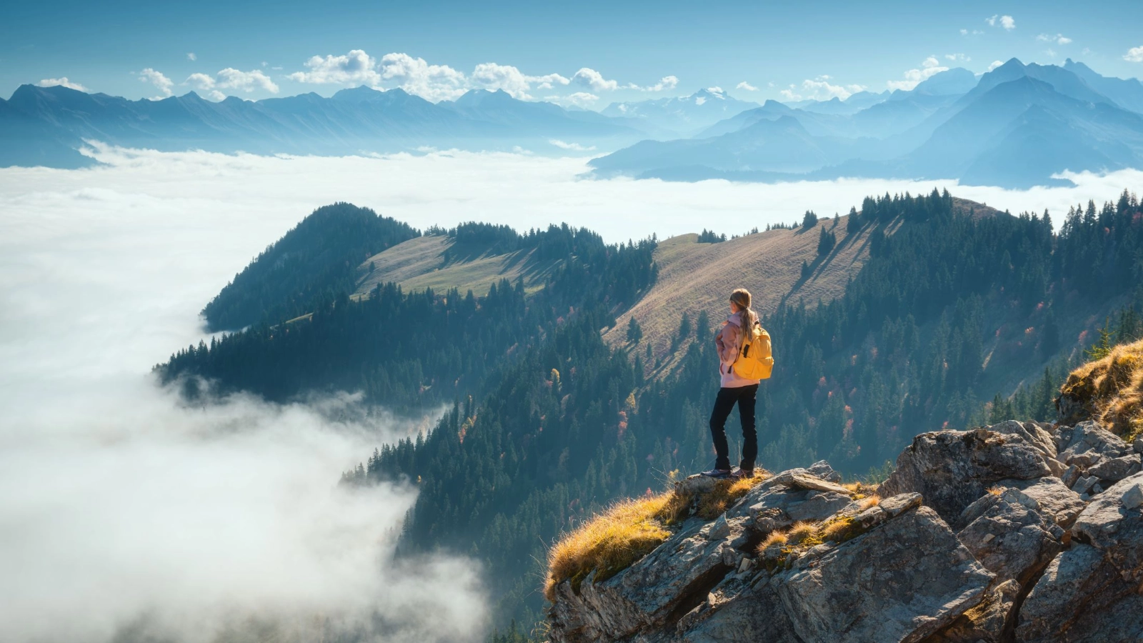 Woman on mountain ridge above a sea of clouds in the Swiss Alps