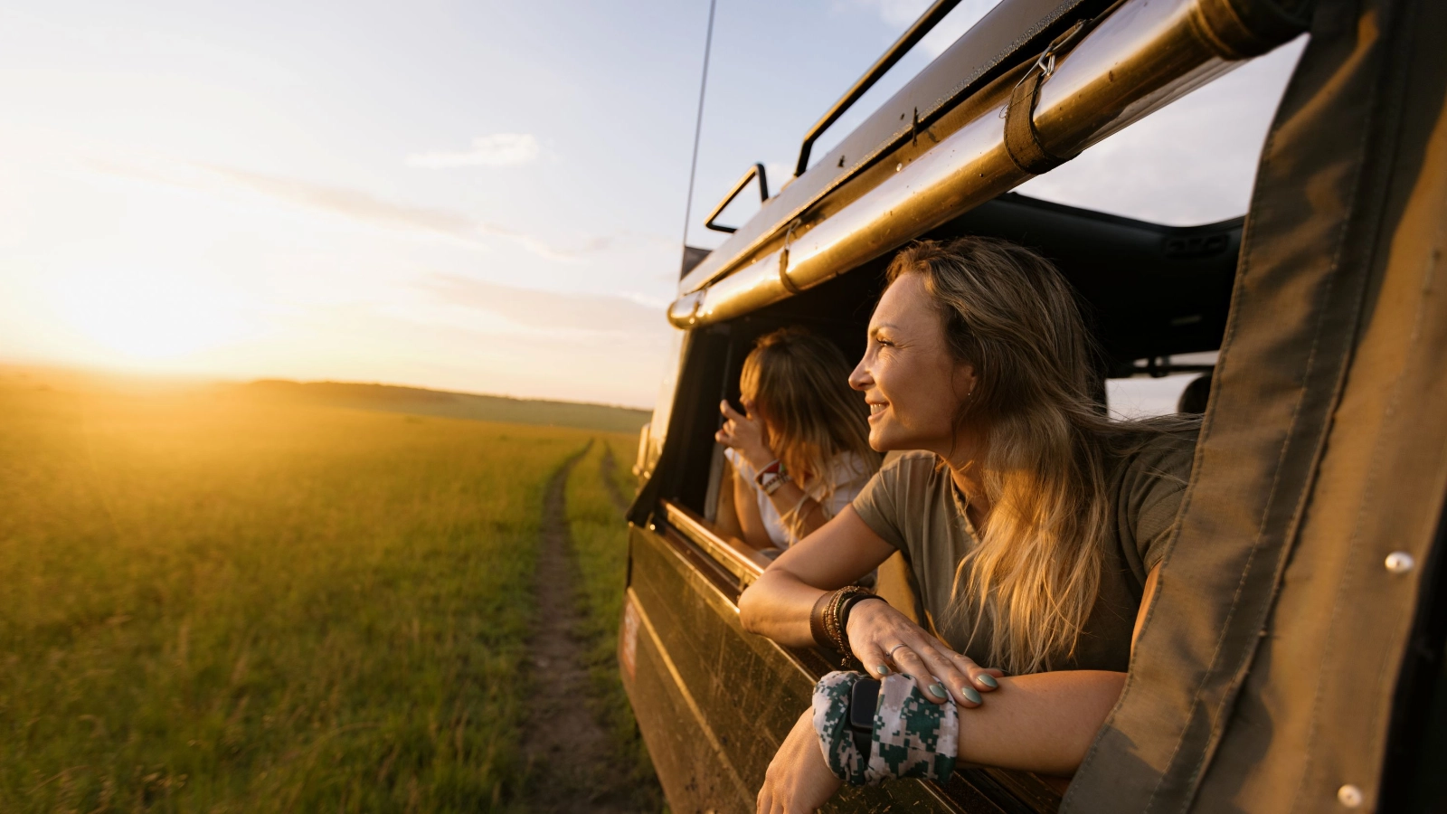 Woman riding in a jeep while enjoying in view of wildlife reserve at sunset.