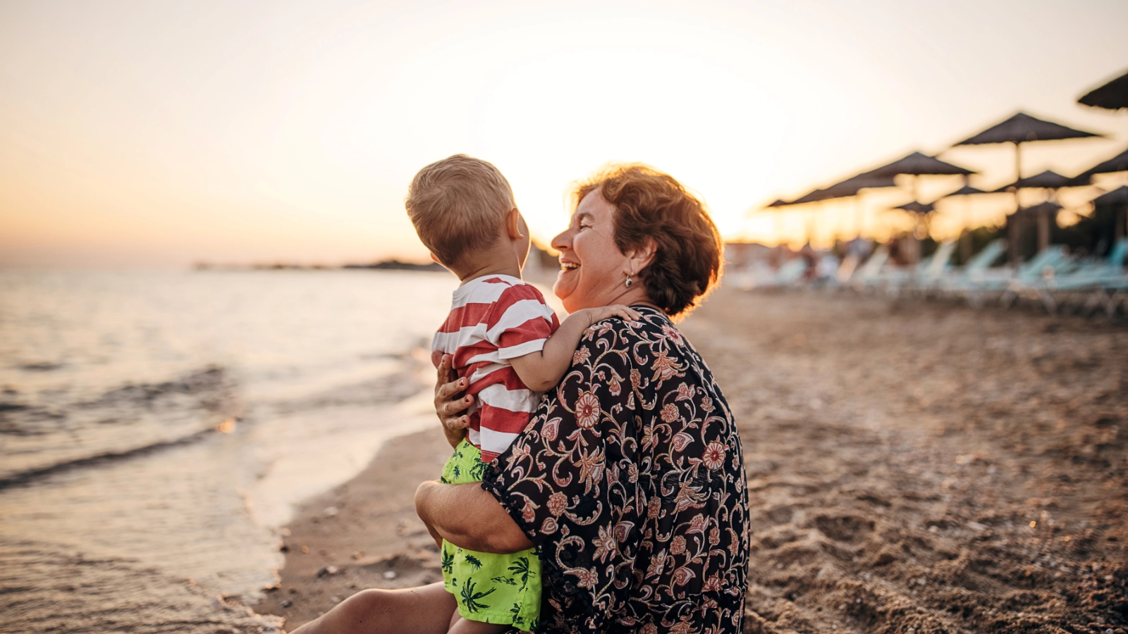A grandparent embracing their grandchild on a sandy beach during sunset