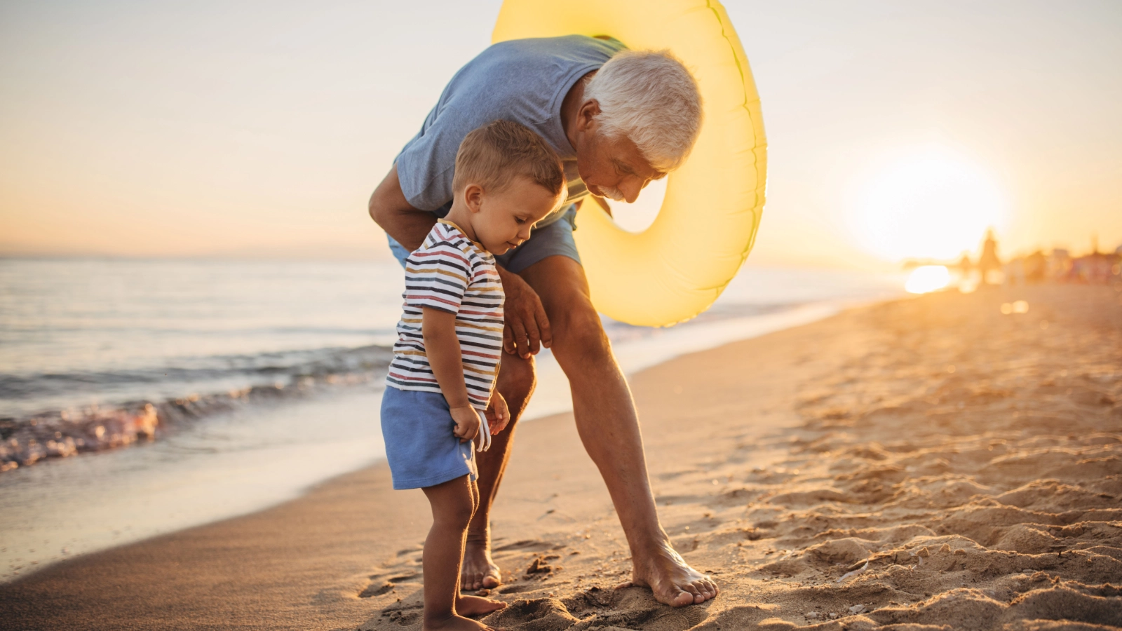 An older adult and a young child enjoying a walk along the beach at sunset.