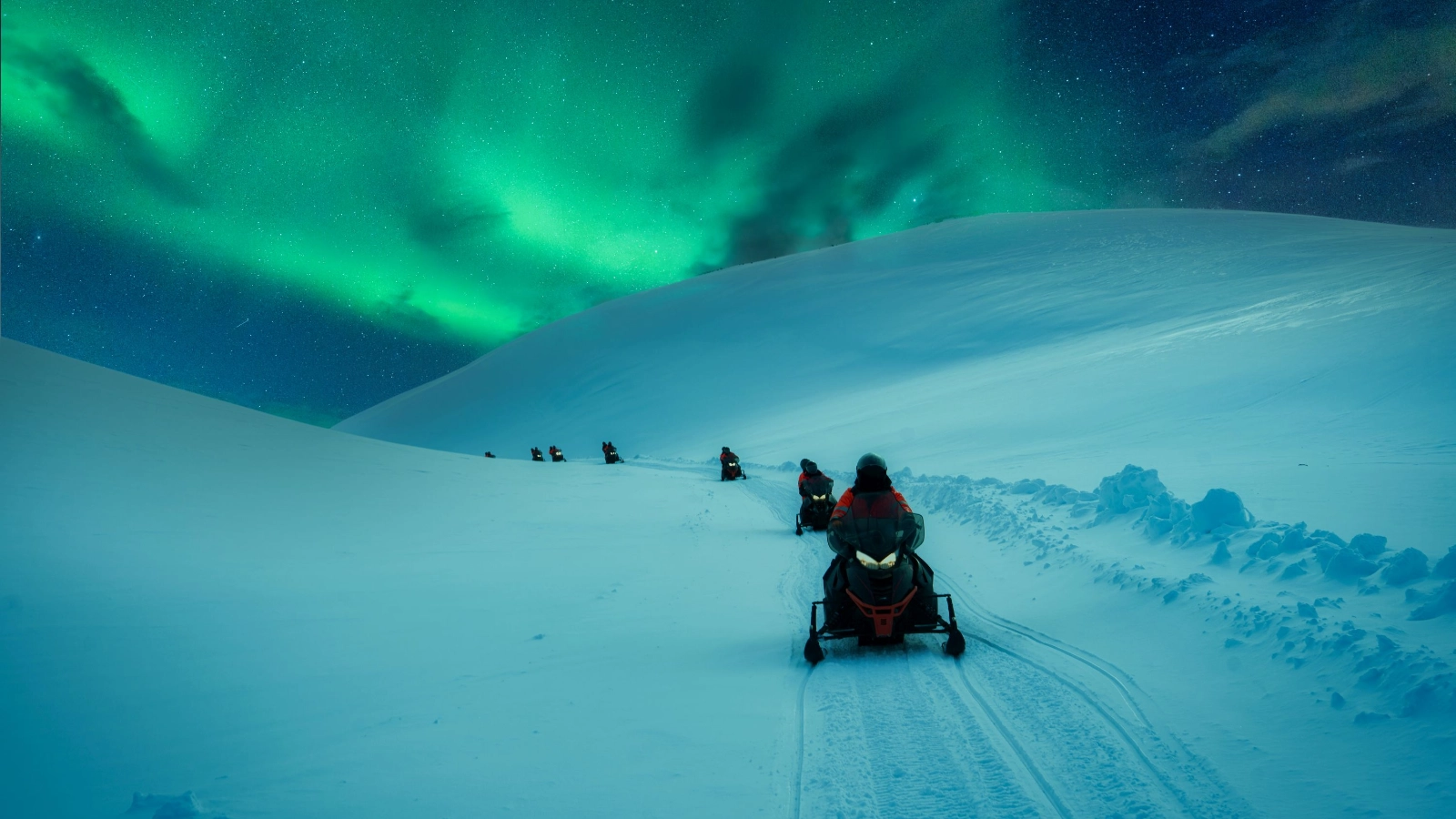 Snowmobile adventure across snowy mountain track with aurora borealis in winter
