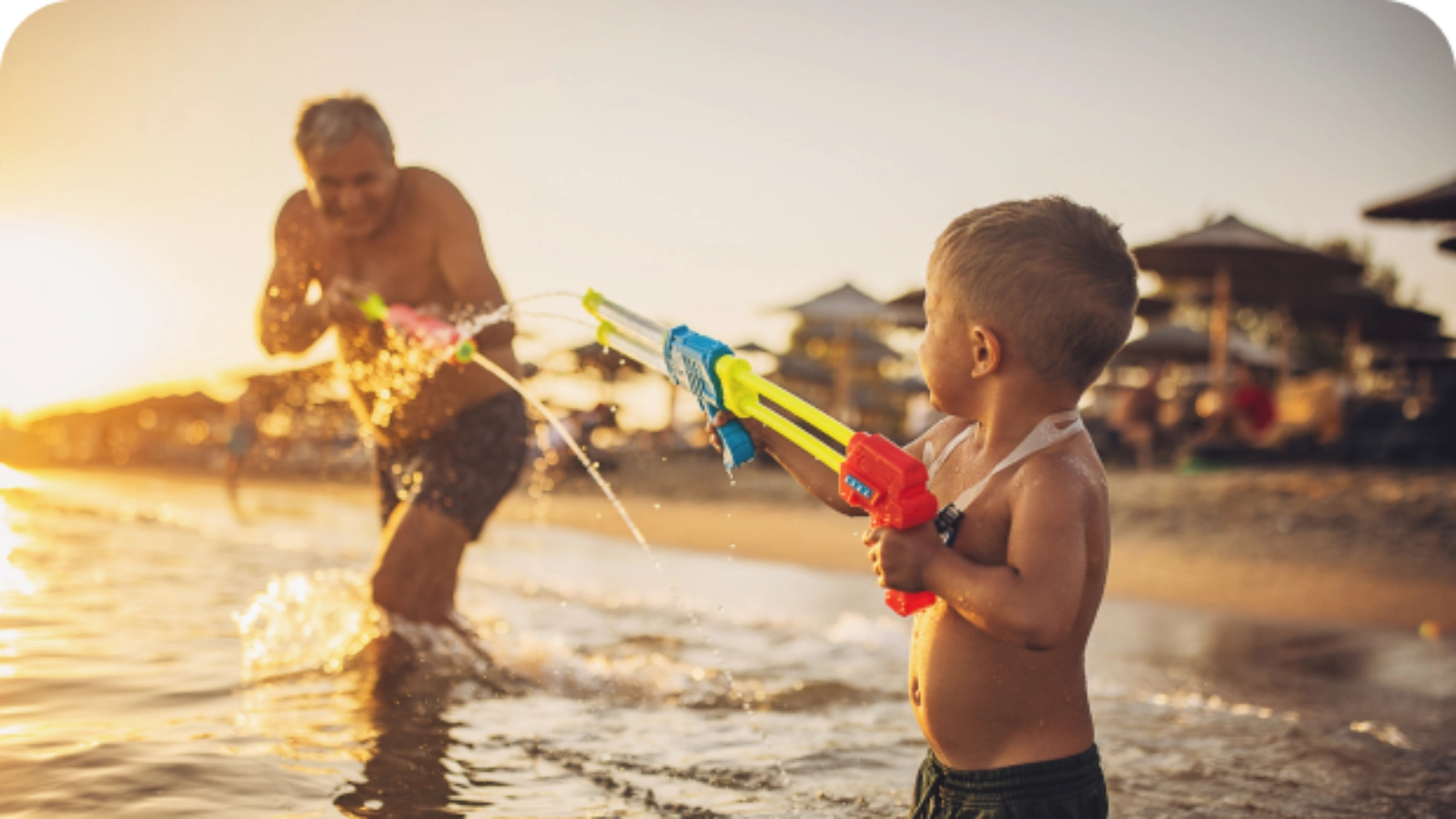 A Grandfather and Grandson playing in the sea with water guns next to the beach