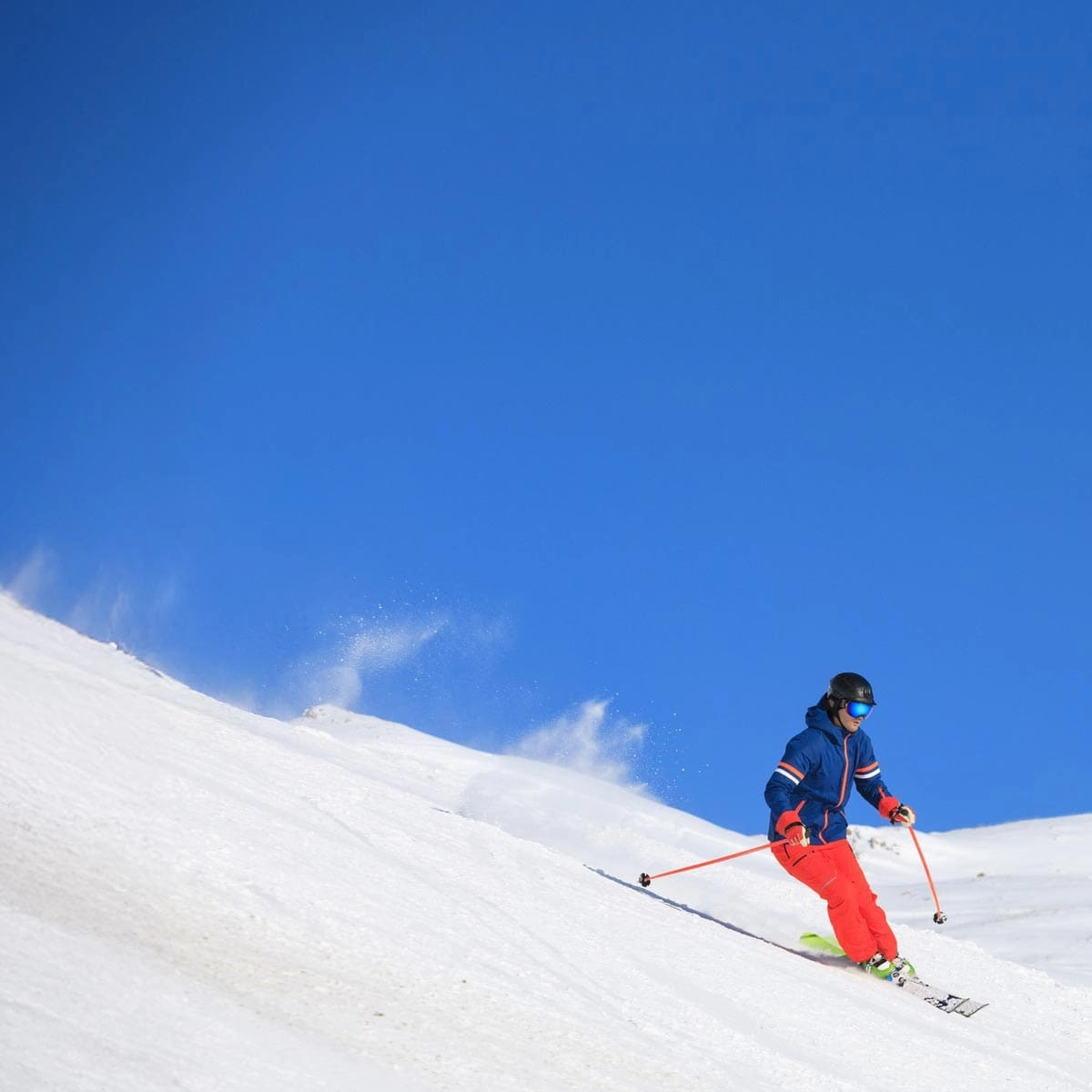 A person skiing in a blue jacket and red trousers